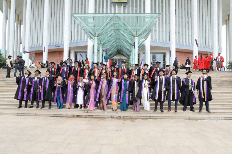 MCAS graduates in academic dress outside a terminal building